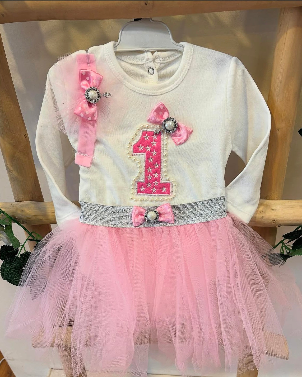 1st Birthday Tutu Set for baby girl: white long-sleeve romper with pink 3-D number 1, pearls and flowers, bows, and pink tutu.